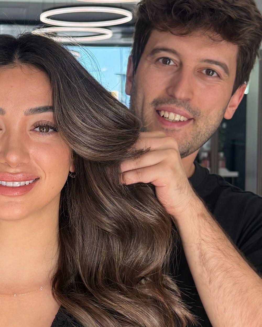 Han Ozmen holding a lock of a client’s brunette hair under the salon’s ring lights